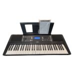 Yamaha electronic keyboard with built-in speakers, control panel, and sheet-music stand with manual on top of the stand