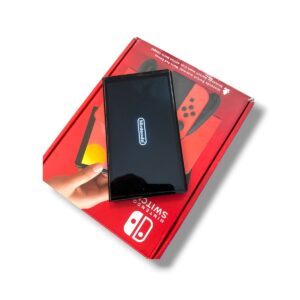Hand holding a black Nintendo Switch screen displaying the Nintendo logo, resting on a red Nintendo Switch box.