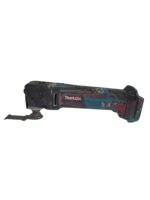 Cordless Makita oscillating multitool covered in dirt with blade attached, lying on its side on a white background