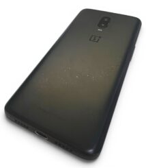 Back of a black OnePlus phone with a dual-camera module and scratches, placed on a white surface.