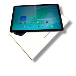 Tablet on a white box, angled view with a blue-green home screen visible on the screen