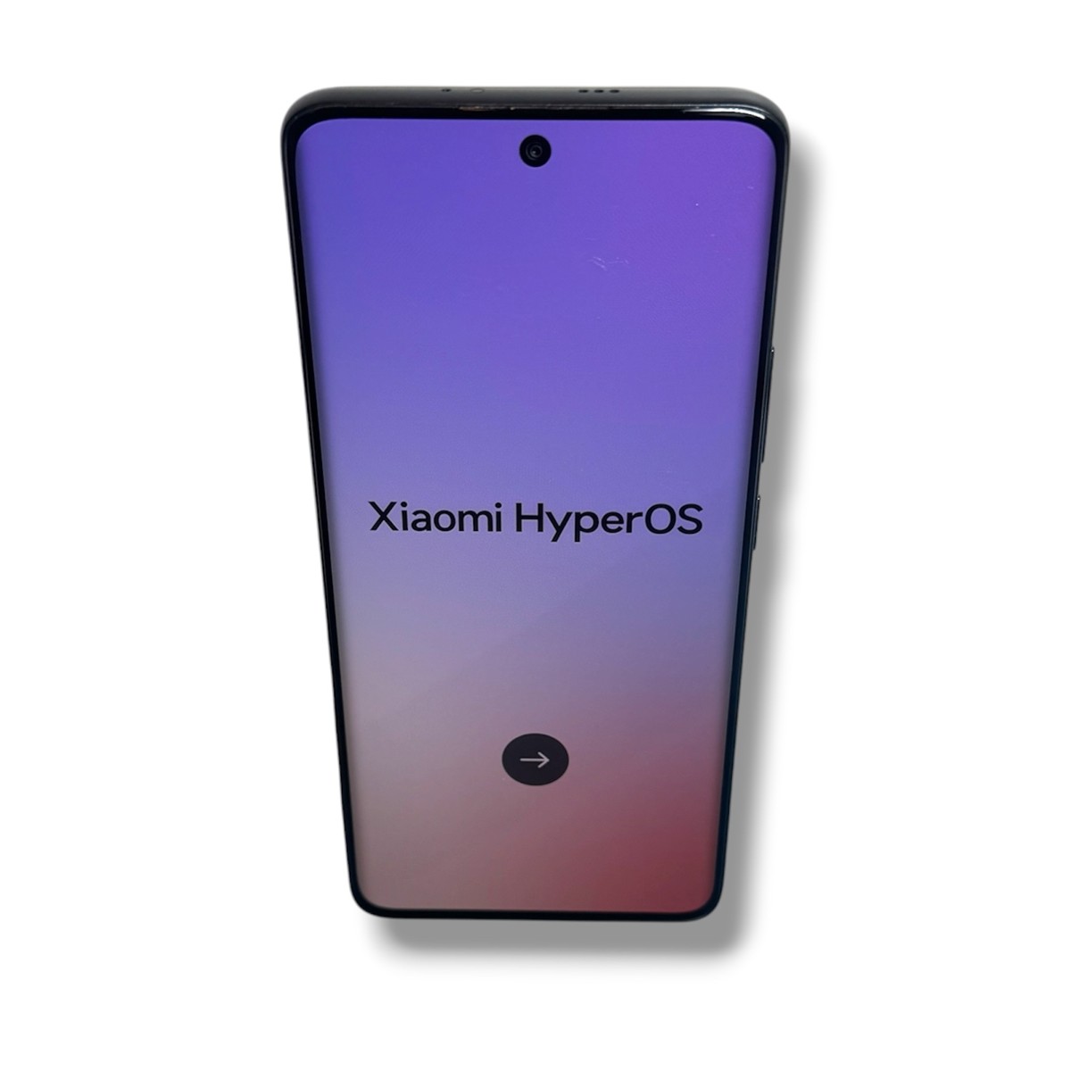 295345b61ddfdd30cf5e44efcb5d1e25jpg - Mezola OÜ Xiaomi smartphone displaying HyperOS branding on a purple-pink gradient screen with a circular forward-arrow button at the bottom left/right area.