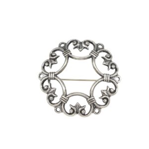 Circular silver decorative brooch finding with ornate scrollwork and a straight pin across the middle.
