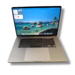 Gold MacBook Pro laptop open, displaying a blue ocean wallpaper with a visible keyboard and large trackpad.