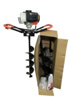Gas-powered earth auger with orange handles and a black helical drill bit, resting beside a cardboard box.
