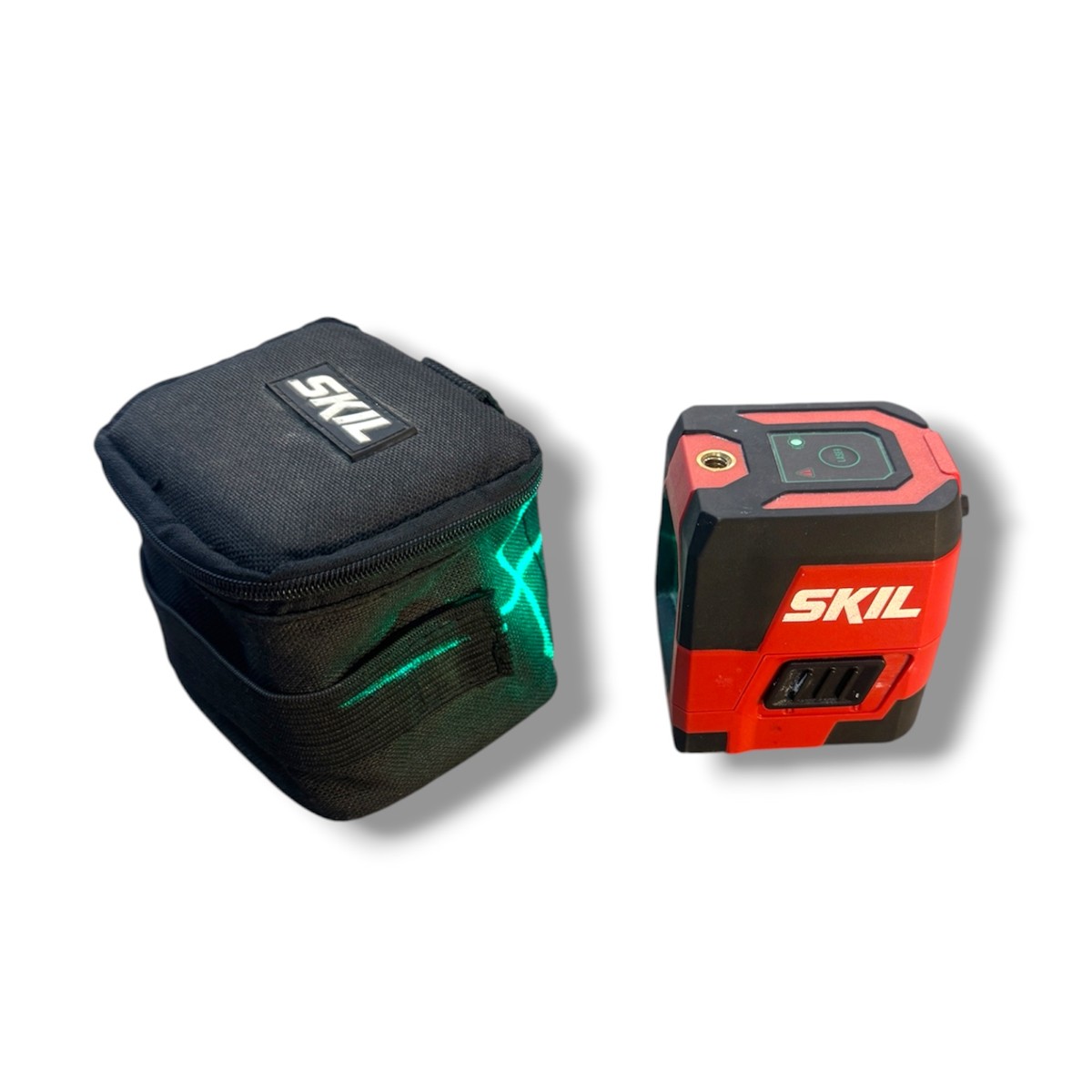 b93998f684d6dfd78cff17c3ab079e3cjpg - Mezola OÜ SKIL laser level (red and black) beside a black SKIL carrying pouch with green laser lines visible on the case area
