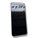 Black smartphone tilted diagonally, screen off and reflecting a blurred sign in the surroundings.