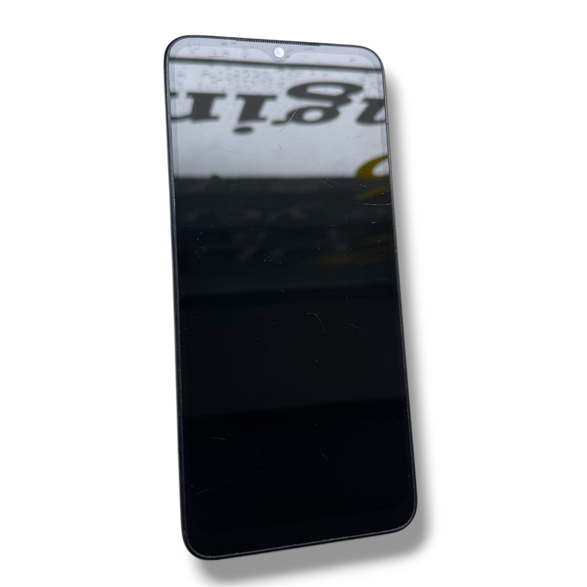 c4dc5a48b763ad8475e5574c8024e40fjpg - Mezola OÜ Black smartphone tilted diagonally, screen off and reflecting a blurred sign in the surroundings.