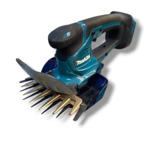 Cordless Makita power tool with a rake-like tine attachment (dethatcher/curved comb) for loosening soil or removing debris.