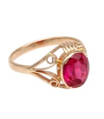 Gold ring with an oval faceted red gemstone set in a decorative filigree band.