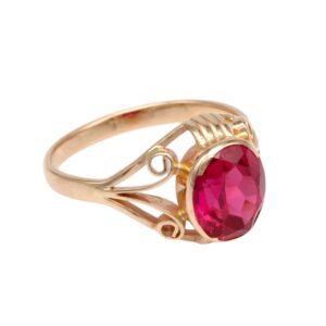 Gold ring with an oval faceted red gemstone set in a decorative filigree band.