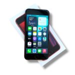 Red-edged iPhone resting on its white box, screen displaying colorful app icons.