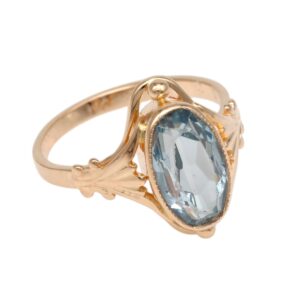 Gold ring with an oval pale-blue gemstone set in an ornate bezel and prongs.