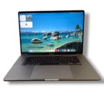 Silver MacBook Pro open to a coastal wallpaper, with the ocean scene on the display and the app dock visible along the bottom edge.