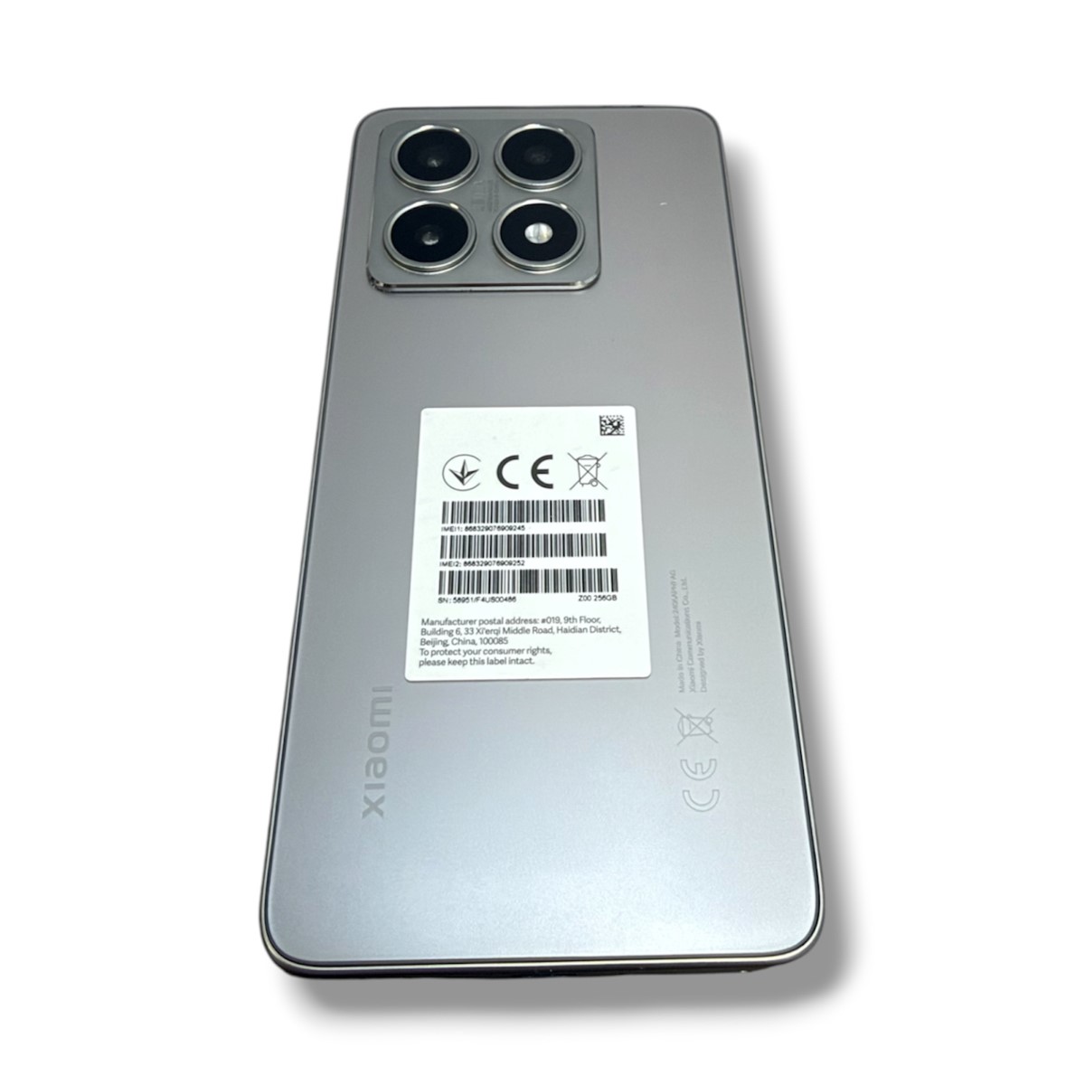 1865e89cebbf249f766c0c0ff4116042jpg - Mezola OÜ Back of a silver Xiaomi smartphone with a quad-camera module and a white barcode label on the center of the back area