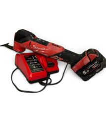 Red cordless drill with a black grip and attached red battery pack on a charger nearby, showing wear from use, Milwaukee branding visible.