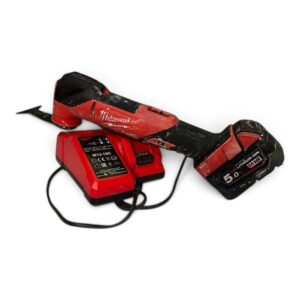 Red cordless drill with a black grip and attached red battery pack on a charger nearby, showing wear from use, Milwaukee branding visible.