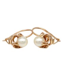 Gold earrings with round white pearls set in ornate openwork hoops on a white background