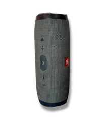 JBL portable speaker in gray fabric with a circular power button and volume controls along the side; cylindrical design with a red JBL logo.