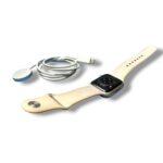 Beige Apple Watch with magnetic charging puck and USB-C charging cable laid nearby